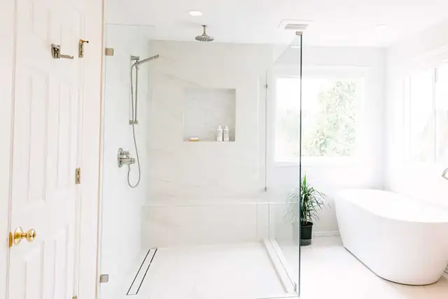 Lake Stevens primary bathroom with a curbless glass shower, linear drain, marble-look wall tile and freestanding soaking tub