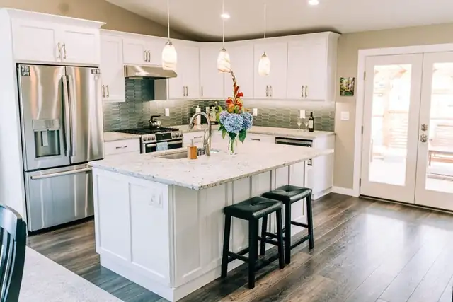 Kitchen remodeling in Marysville, WA: white Shaker cabinets, a granite-topped island with black stools, stainless appliances and green glass tile backsplash