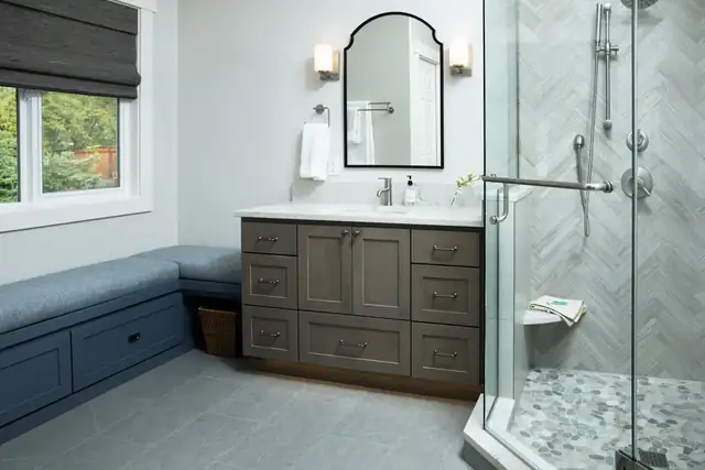 Luxury primary bathroom remodel in Snohomish, WA with a gray wood vanity, built-in window bench and herringbone-tiled glass shower