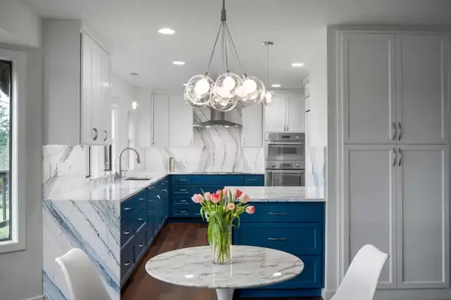 Modern blue kitchen remodel in Snohomish, WA with a statement waterfall stone countertop, white upper cabinets and a round marble table