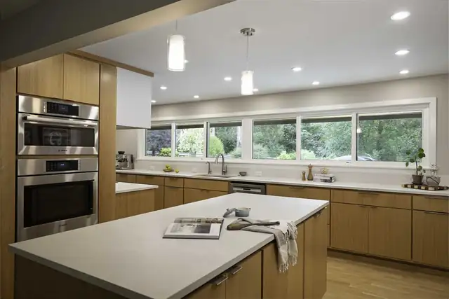 Universal design kitchen with wood cabinets, wall ovens at an easy reach height, a wide white island and a long window wall