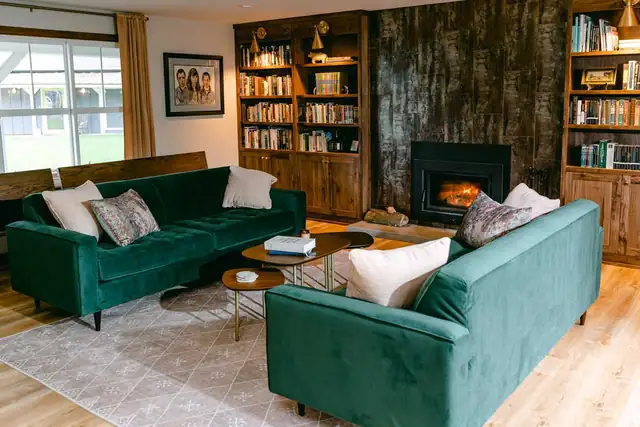 Whole home remodel living room with green velvet sofas, built-in wood bookshelves and a tiled fireplace insert
